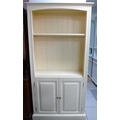 A modern cream painted bookcase, with two adjustable shelves and cupboard below.