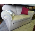A modern two seater sofa, diamond patterned beige fabric upholstery, scroll arms and shaped back.