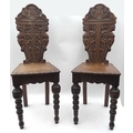 A pair of Victorian Arts and Crafts style oak hall chairs with carved backs and caryatyd sides aroun... 