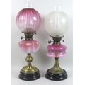 Two Victorian oil lamps, with pink pink glass reservoirs, painted decoration, brass columns and blac... 