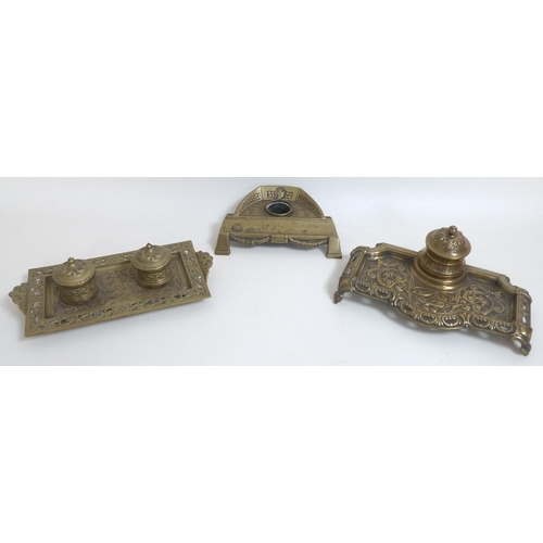 83 - A group of three brass desk stands, each with cast decoration, one with twin inkwells on tray shaped... 