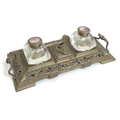A Victorian brass desk stand, with twin cut glass inkwells, central lidded compartment with snake ha... 