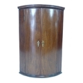 A George III mahogany bow fronted corner cupboard, with double doors enclosing three fixed shelves, ... 