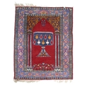 A Persian prayer rug with red ground, with mihrab arch centred by various hanging urns to a shaped m... 