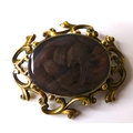 A Victorian yellow metal mourning brooch, with scrolling frame around a glazed oval window set with ... 