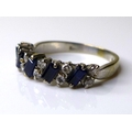 An 18ct white gold, dark sapphire and diamond ring, five baguette cut stones, each 4 by 2mm, set alt... 