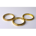 A group of three gold wedding bands, two 9ct gold, sizes L/M, 5.7g combined, and one yellow metal wi... 
