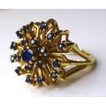 A 14ct gold and sapphire dress ring, the central round cut stone surrounded by eighteen smaller ston... 