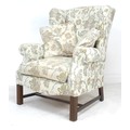 A modern Georgian style wing armchair, upholstered in cream and pale colours, floral and foliate pat... 