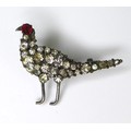 A paste set brooch in the form of a pheasant, with white metal legs and beak, red stone forming the ... 