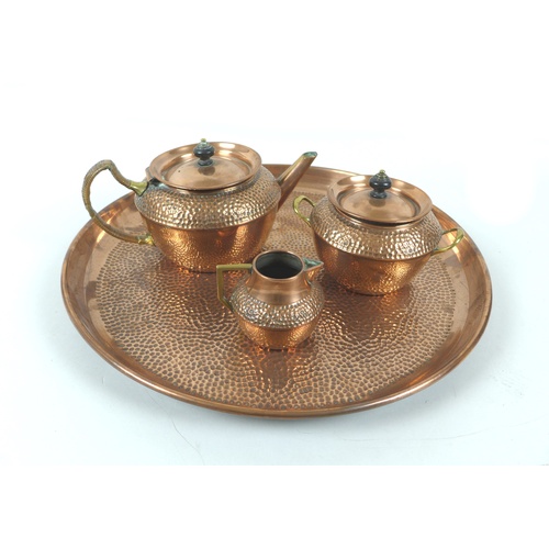 93 - An Arts & Crafts four piece planished copper tea set, comprising tray, teapot, covered sugar bowl an... 