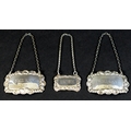 A group of three silver decanter labels, each with cast foliate decorative borders, comprising a sma... 