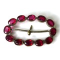 A decorative buckle set with twelve magenta coloured oval 'stones', each 7 by 5 by 3mm, possibly Geo... 