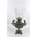 A Victorian cast metal paraffin lamp, with clear glass reservoir on a cast base, decorated in relief... 