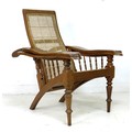 A teak and cane backed reclining planters chair, the arms with spindle support and swivel foot rests... 