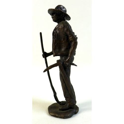 95 - A bronze sculpture of a miner, the man dressed in working clothes carrying a pickaxe in one hand and... 