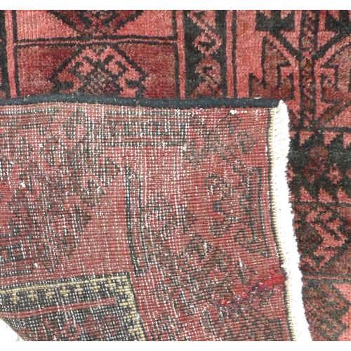 304 - A Baluchi rug with red ground, fifteen black geometric panels to the field, with thin white cross mo... 