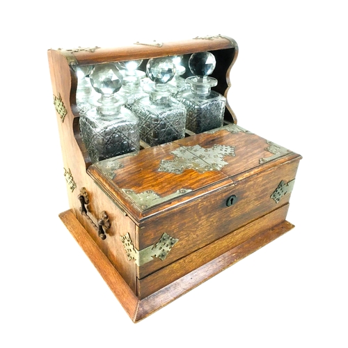 85 - A late 19th century oak tantalus with three decanter bottles, a lidded front compartment with secret... 