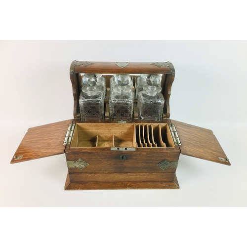 85 - A late 19th century oak tantalus with three decanter bottles, a lidded front compartment with secret... 