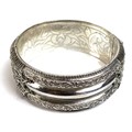 A finely worked broad bangle of Indian style design, the white metal with foliate scrolls, beading a... 