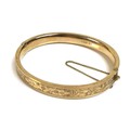 A 9ct gold bangle, with floral bright cut engraved decoration, complete with safety chain, 13.2g tot... 