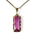 A 14ct gold pink sapphire pendant, the emerald cut pink sapphire 20 by 8mm, with 14ct gold rococo fo... 