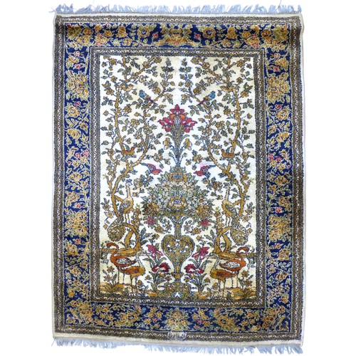 307 - A Kirman Tree of Life rug, cream ground, dark blue border, decorated with oranges, greens, reds, and... 