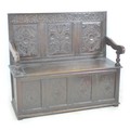 An 18th century oak settle, with carved frieze above a three panel carved back, open shaped armrests... 