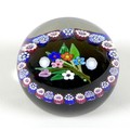 A Paul Ysart style paperweight, the black ground with posy of spring flowers to the centre, bordered... 