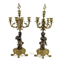 A pair of bronze and gilt metal candelabra, each modelled as a putto holding an urn below a four bra... 