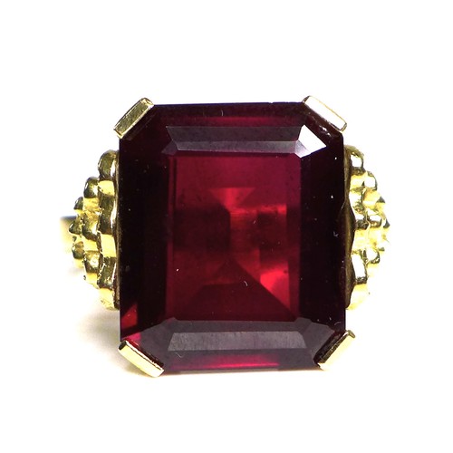 231 - A Middle Eastern gold and imitation ruby dress ring, the emerald cut red stone, 40 by 20 by 5mm, in ... 