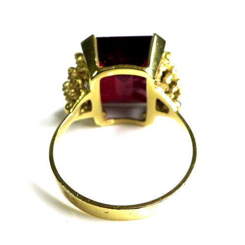 231 - A Middle Eastern gold and imitation ruby dress ring, the emerald cut red stone, 40 by 20 by 5mm, in ... 