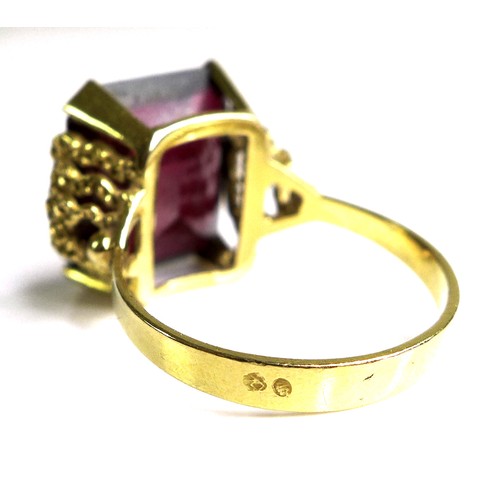 231 - A Middle Eastern gold and imitation ruby dress ring, the emerald cut red stone, 40 by 20 by 5mm, in ... 