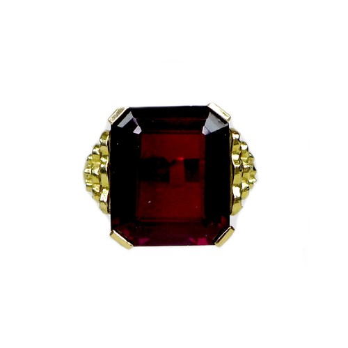 231 - A Middle Eastern gold and imitation ruby dress ring, the emerald cut red stone, 40 by 20 by 5mm, in ... 