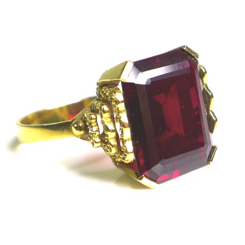 231 - A Middle Eastern gold and imitation ruby dress ring, the emerald cut red stone, 40 by 20 by 5mm, in ... 