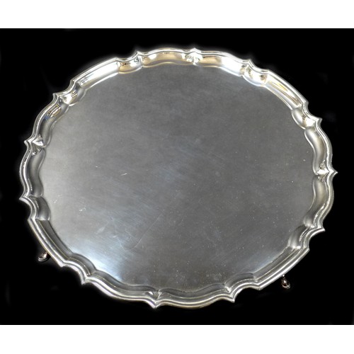 28 - An Edwardian silver tray, of circular form with Chippendale pie crust edge, raised on four stepped h... 