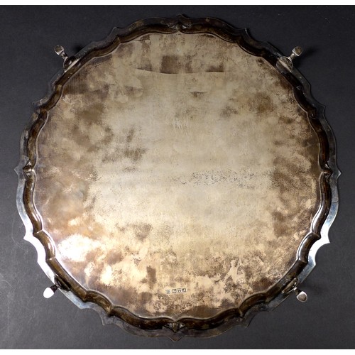 28 - An Edwardian silver tray, of circular form with Chippendale pie crust edge, raised on four stepped h... 