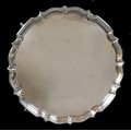 An Edwardian silver tray, of circular form with Chippendale pie crust edge, raised on four stepped h... 