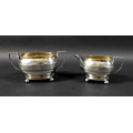 A George III silver twin handled sugar bowl and cream jug, the rectangular casket form bodies decora... 