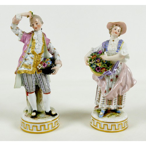 A pair of Meissen porcelain figures, mid 19th century, modelled as flower sellers, model numbers C72 and C73, after the originals modelled by Acier, he with flowers in his upturned hat and a single bloom in his raised hand, she with flowers in her basket suspended from a ribbon around her neck, both dressed in 18th century attire, on raised circular bases with relief moulded and gilt lined Greek key pattern frieze, both with underglaze blue crossed swords mark, the man incised 'C 73', impressed '124', and painted '19', 6 by 17cm high, the lady incised 'C 72', impressed '115' and '133', and painted '19', 6 by 16cm high. (2)