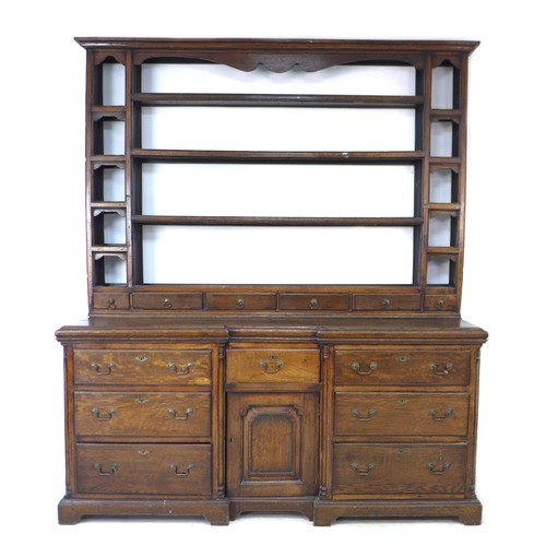 A George II oak dresser, the rack with three shelves above six short drawers flanked by compartments, shaped aprons, the break front base with three cupboard doors, raised on bracket feet, 66 by 183 by 215cm high.