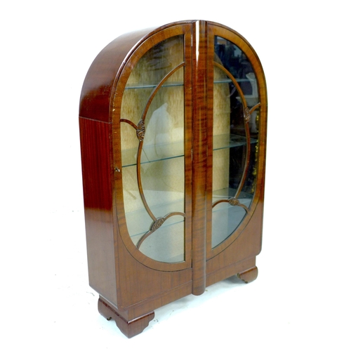 256 - A 1930s oak veneered bookcase,  with domed top and twin glazed doors, enclosing three adjustable she... 