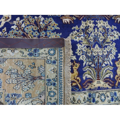 296 - A part silk Qum rug on cream ground, with deep blue central panel depicting a still life of birds an... 