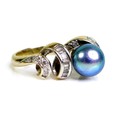 An 18ct gold black pearl and diamond ring, the pearl of approximately 7.5mm diameter, within a scrol... 