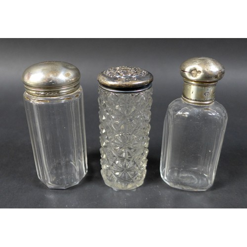 28 - A collection of six silver-topped glass bottles, including two small jars with floral-patterned tops... 