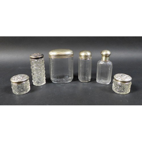 28 - A collection of six silver-topped glass bottles, including two small jars with floral-patterned tops... 