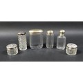 A collection of six silver-topped glass bottles, including two small jars with floral-patterned tops... 