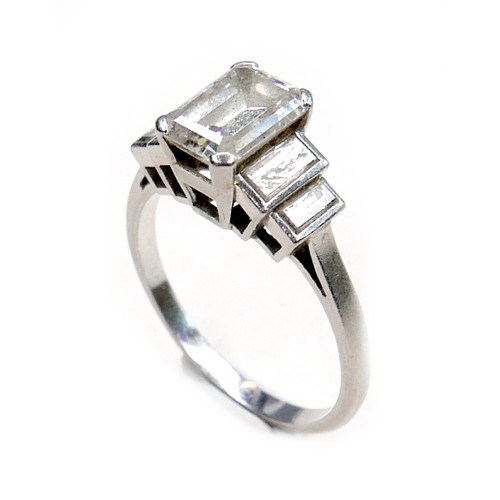 392 - An Art Deco style white gold and platinum diamond ring, the central emerald cut stone of 7.7 by 5.5 ... 