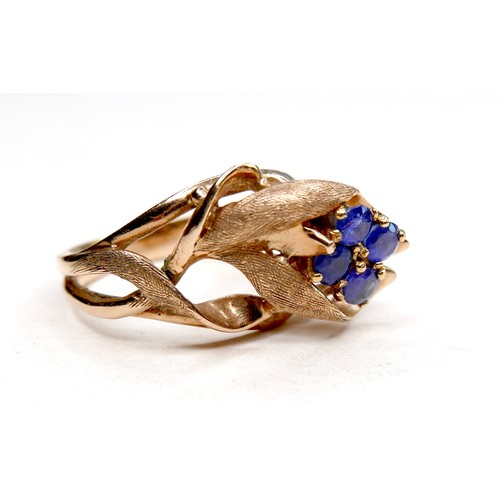 260 - A gold dress ring in the form of a flower, set with four small cornflower blue sapphires, marks rubb... 