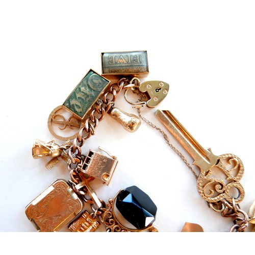 390 - A 9ct rose gold charm bracelet, kerb link with heart padlock clasp, fitted with twenty-one mostly 9c... 